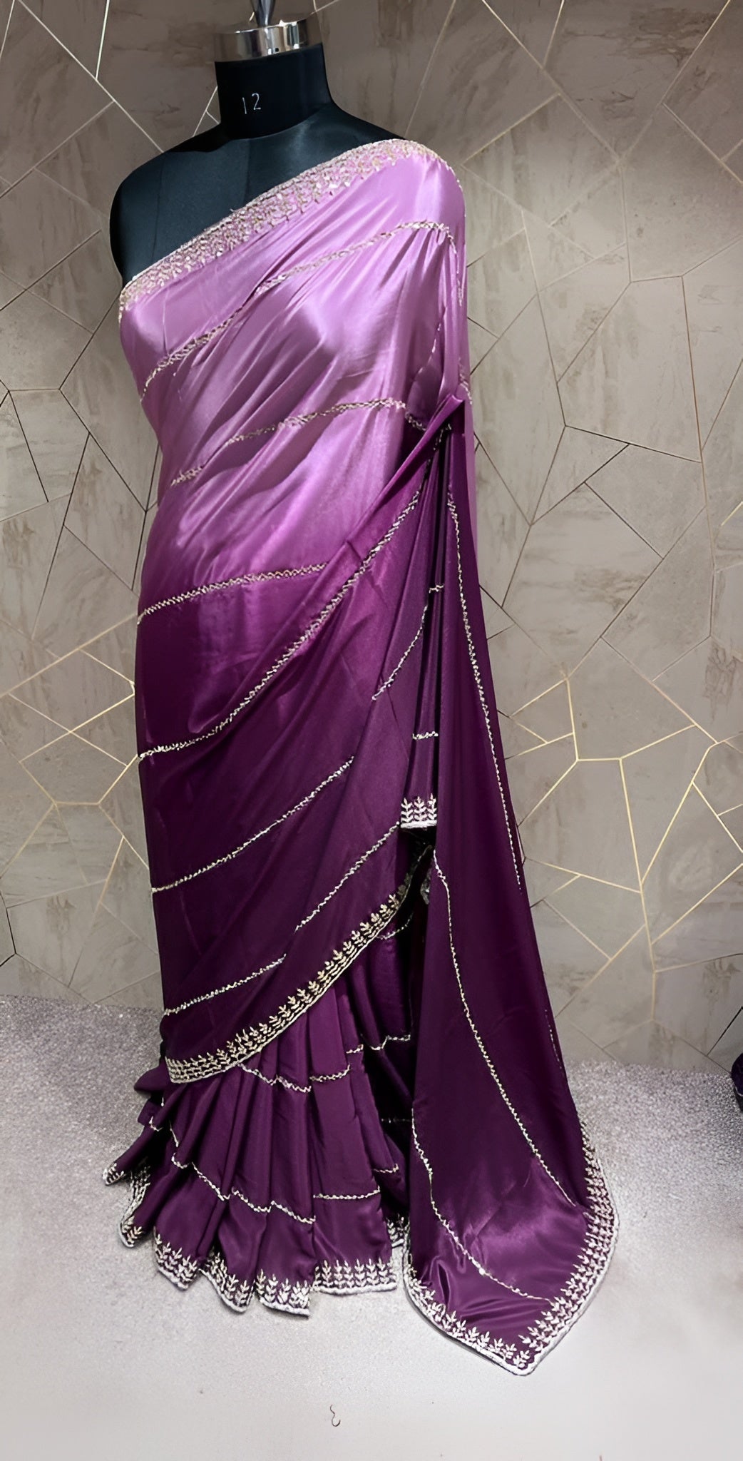 Purple saree with silver border on a mannequin against a textured wall.